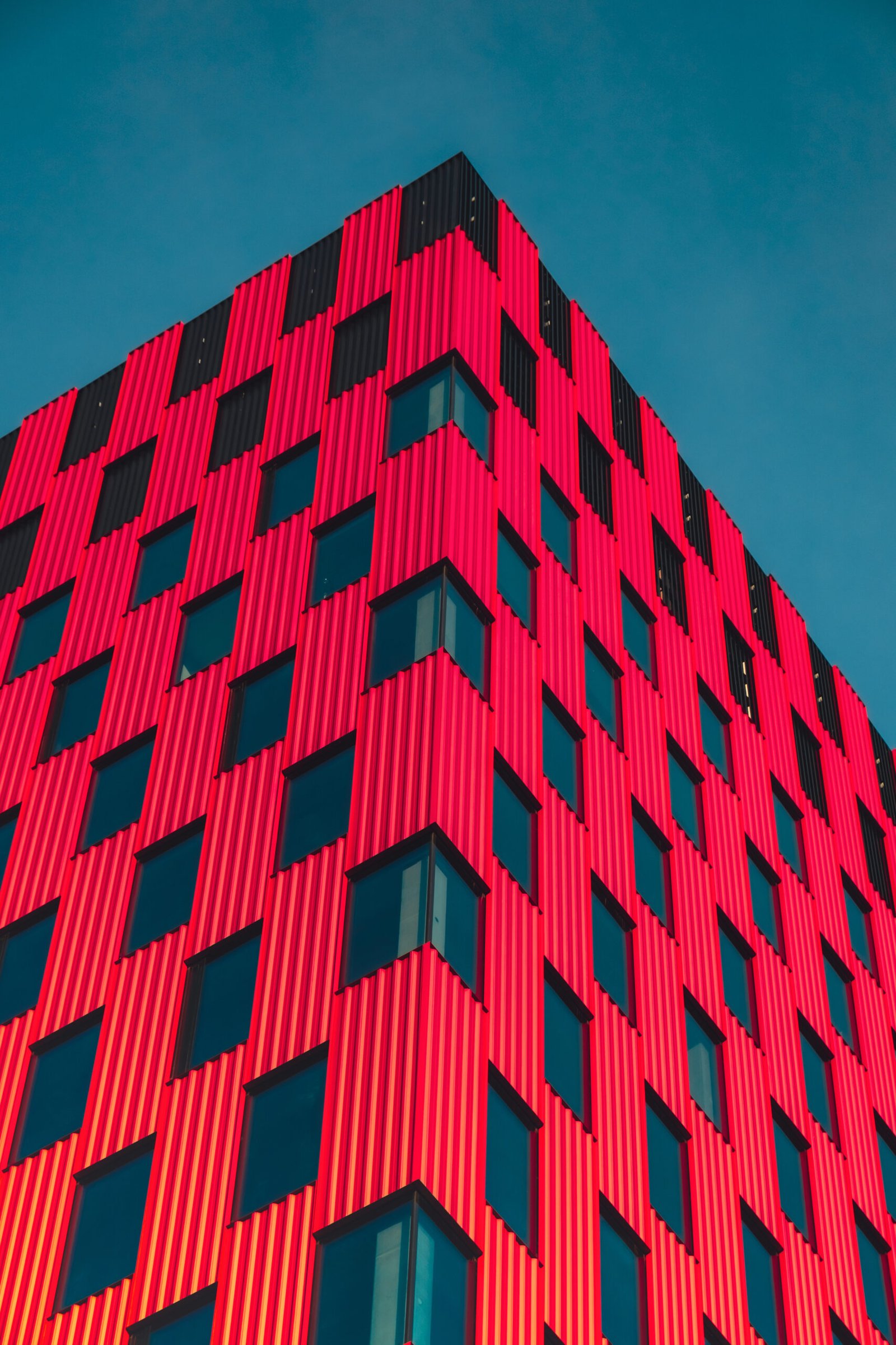 modern office building exterior with glass facade on clear sky background. vivid colors transparent glass wall of office building with red pink decoration. element of facade of modern european building commercial office buildings. abstract